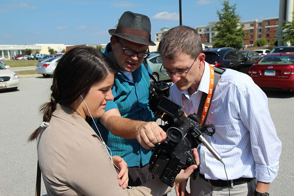 Three people watch playback of filming on a camera