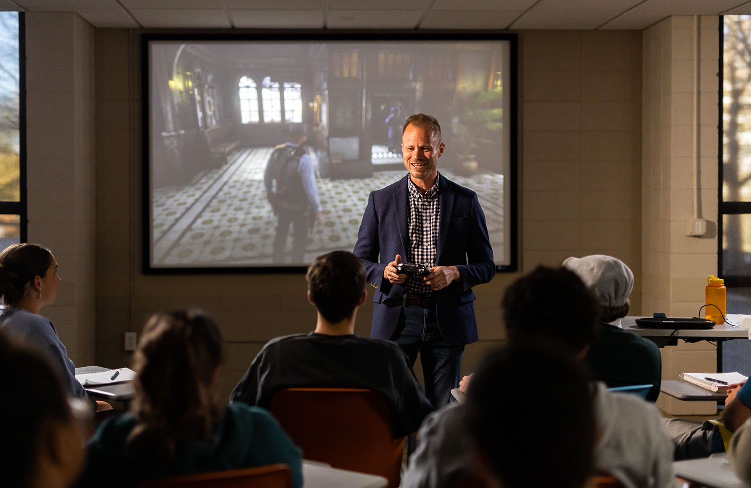 Tore Olsson stands in front of a screen displaying a scene from the game Red Dead Redemption II with a classroom of students observing.